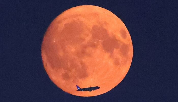An aircraft crosses the moon with a red glow caused by North American wildfire smoke, seen from Parliament Hill, London, August 18, 2024. — Reuters