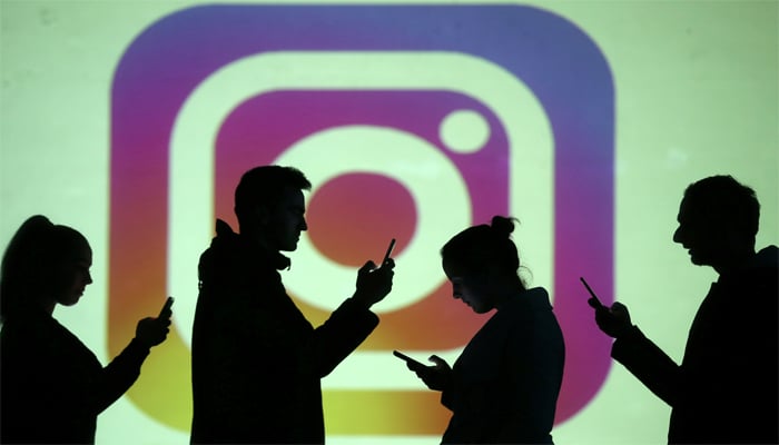 Silhouettes of mobile users are seen next to a screen projection of Instagram logo in this picture illustration taken March 28, 2018. — Reuters