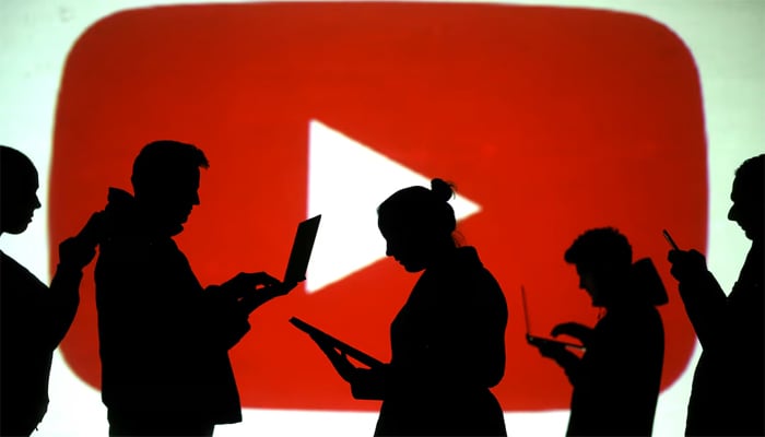 Silhouettes of laptop and mobile device users are seen next to a screen projection of YouTube logo in this picture illustration taken March 28, 2018. — Reuters