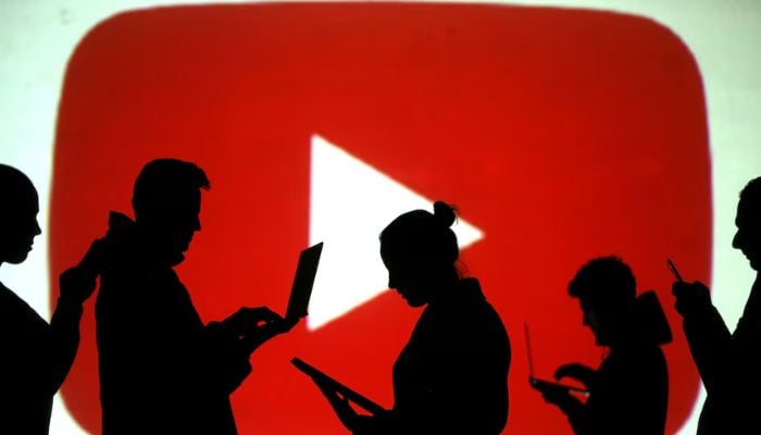 An image of silhouettes of laptop and mobile device users is seen next to a screen projection of the YouTube logo in this picture illustration taken March 28, 2018. — Reuters