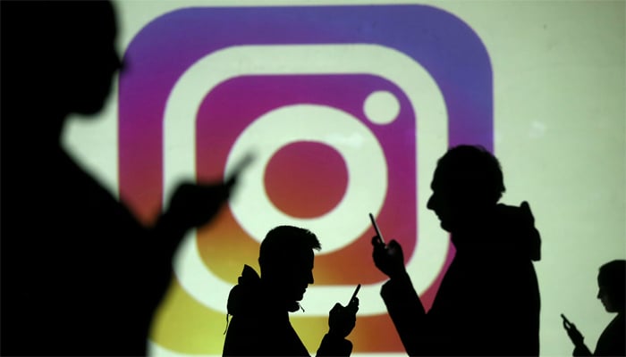 Silhouettes of mobile users are seen next to a screen projection of the Instagram logo in this picture illustration taken March 28, 2018. — Reuters