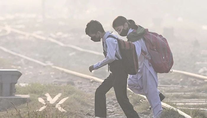 An image of schoolchildren wearing masks walking across a railway track amid thick smog in Lahore on November 20, 2024. — AFP