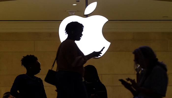 A women uses an iPhone mobile device as she passes a lighted Apple logo at the Apple store at Grand Central Terminal in New York City, US, April 14, 2023. — Reuters