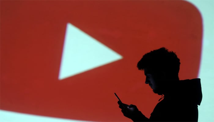 A silhouette of mobile user is seen next to screen projection of YouTube logo in this picture illustration taken March 28, 2018. — Reuters