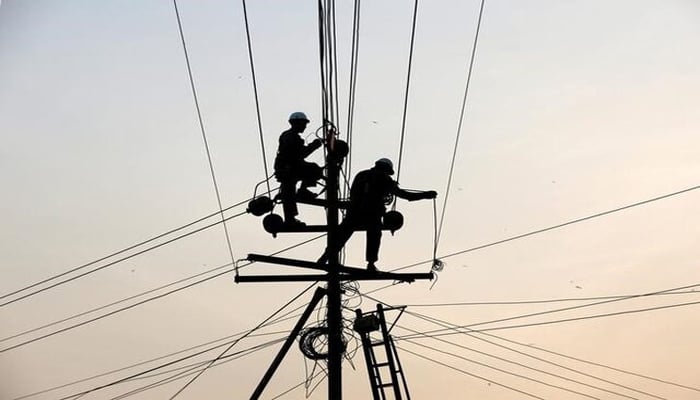 Technicians are silhouetted as they fix cables on a power transmission line in Karachi, Pakistan January 9, 2017. — Reuters