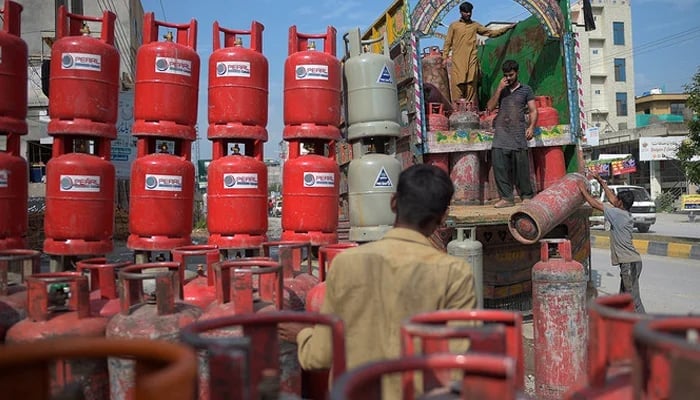 An undated image showing Labourers unloading gas cylinders from a truck at a market on the outskirts of Islamabad. — AFP