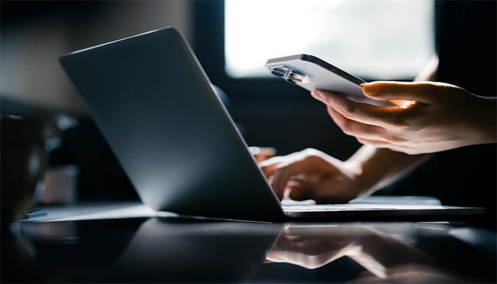 An undated image of person using iPhone and laptop. — Getty Images