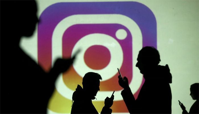 Silhouettes of mobile users are seen next to a screen projection of the Instagram logo in this picture illustration taken March 28, 2018. — Reuters