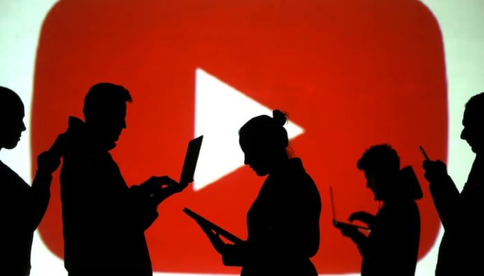 Silhouettes of laptop and mobile device users are seen next to a screen projection of Youtube logo in this picture illustration taken March 28, 2018. — Reuters